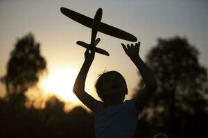 contento niño obras de teatro con un avión a puesta de sol. silueta de un chico con un avión en el antecedentes de el Dom. foto