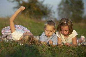 Sisters and little brother lie on the grass. Children play in the meadow. A happy family. photo