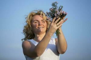 Beautiful middle-aged blonde with a bouquet of wildflowers against the blue sky. photo