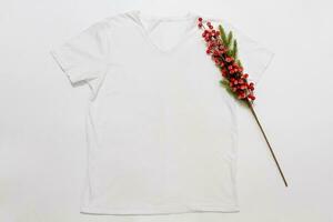 Close up white blank template t shirt with copy space and Christmas Holiday concept. Top view mockup t-shirt and red holidays decorations on white background. Happy New Year accessories. Xmas outfit photo