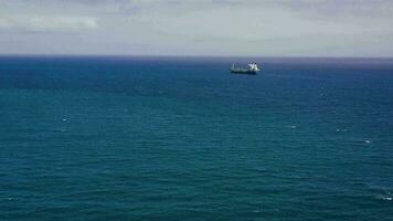 Aerial view of a sea vessel for transportation of a dry-cargo ship with a closed hold is anchored near the seaport city and awaits unloading. Import and export by sea. Smooth water and clear sky video