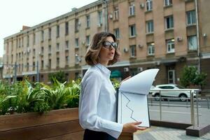 mujer gerente en blanco camisa al aire libre con documentos foto