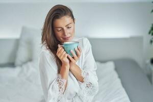 Brunette woman on bad in pajama with mug with coffee or tea photo