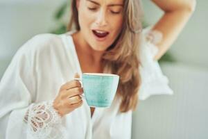 Brunette woman on bad in pajama with mug with coffee or tea photo