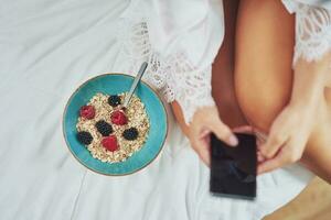 Nice brunette on bed wit cereal breakfast with phone photo