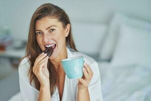 bonito joven sexy mujer con taza y Galleta terminado cama foto