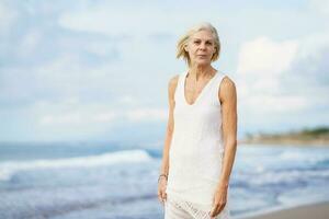 Smiling mature woman walking on the beach. Elderly female standing at a seaside location photo