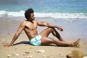 Black man in swimsuit sitting on sandy beach photo