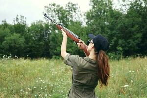 Military woman holding gun up sight hunting back view fresh air green photo