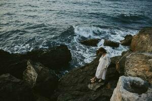 novia en un vestir con mojado pelo en el rocoso piedras cerca el Oceano foto