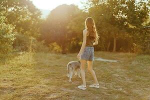 un mujer carreras su espalda a el cámara con un perro en el bosque durante un noche caminar en el bosque a puesta de sol en otoño. estilo de vida Deportes formación con tu amado perro foto