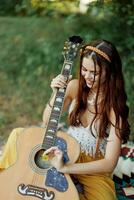 contento hippie mujer con un guitarra relajante en naturaleza sentado en un tartán sonriente y disfrutando el vista. estilo de vida en armonía con naturaleza y yo foto
