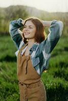 retrato de un joven niña en un verano día en el rayos de el ajuste Dom con un hermosa sonrisa, vestido como un granjero y jardinero foto
