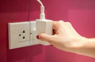 Hand is unplug the electric line off a white socket on the red wall. photo