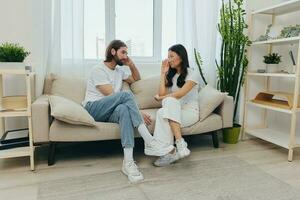 A man and a woman of different races sit on the couch in a room at home and talk about their problems to each other. A stress-free lifestyle of family quarrels with psychological support photo