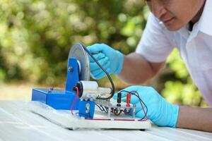 Close up hands wear blue gloves demonstrate science experiment about electricity circuit from dynamo kit for teaching. Concept, science subject, project work. Experiment, education. Outdoor class photo