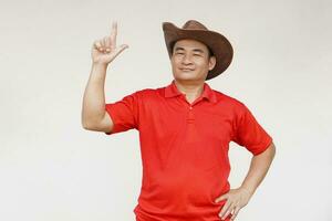 Asian man wears hat, red shirt, pose hand on waist, point finger up, feels confident. Copy space of adding text or advertisement. photo