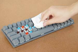 Closeup hand use tissue paper to clean wireless computer keyboard. Concept hygiene and disinfection on computer device that may have dust, germs, bacteria or virus on it photo