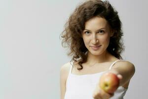 Smiling lovely cute curly beautiful woman in basic white t-shirt pulls apple enjoy healthy food posing isolated on over white background. Natural Eco-friendly products concept. Copy space photo