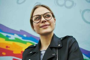 contento mujer en un cuero chaqueta y lentes cerca el multicolor pintada en el pared foto