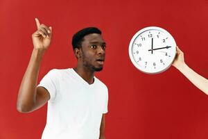 emocional africano americano siguiente a el reloj gesticulando con su mano estudio foto