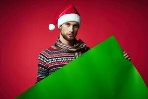 Cheerful man in a santa hat holding a banner holiday red background photo