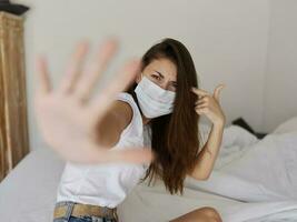 woman in medical mask covers camera with hand indoors quarantine pandemic coronavirus photo