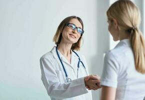 woman doctor shakes hands with patient in white t-shirt photo