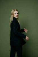 An amazing stunning stylish girl in a designer suit turns in motion looks at you in the camera posing on a green olive background in the studio photo