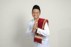 Portrait of attractive Asian muslim man in white shirt with skullcap showing apologize and welcome hand gesture. Isolated image on gray background photo