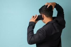 Portrait of young Asian business man in casual suit facing side while confused gestures talking with someone in phone. Isolated image on blue background photo