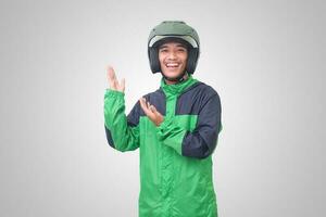 Portrait of Asian online taxi driver wearing green jacket and helmet pointing at empty space with finger. Isolated image on white background photo