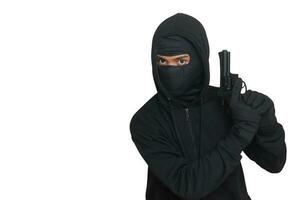 Mysterious man wearing black hoodie and mask holding a pistol, shooting with a gun. Isolated image on gray background photo