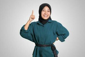 Portrait of excited Asian hijab woman in casual shirt pointing up her forefinger and reminding something to do. Advertising concept. Isolated image on white background photo