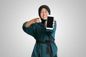 Portrait of excited Asian muslim woman with hijab showing and presenting blank screen mobile phone. Advertising mock up concept. Isolated image on white background photo