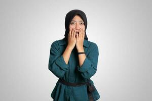 Oh my god Portrait of surprised Asian muslim woman in casual shirt looking at camera with shocked eyes and holding hands on cheeks. Isolated image on white background photo