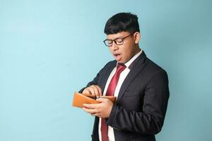 Portrait of young Asian business man in casual suit looked surprised while holding empty leather wallet. Isolated image on blue background photo