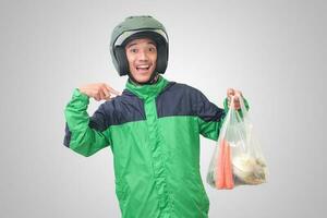 Portrait of Asian online taxi driver wearing green jacket and helmet delivering the vegetables from traditional market and pointing with finger. Isolated image on white background photo