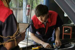 dos profesional automotor mecánico socios cheque y reparar un ev coche batería y híbrido motor a un mantenimiento cochera, experto eléctrico vehículo servicio, y fijación ocupaciones auto industria. foto