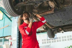 auto mecánico trabajando en cochera, técnico hombre trabajando en auto Servicio con levantado vehículo, coche reparar, y mantenimiento foto