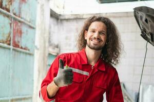 Portrait of a young car mechanic showing thumbs up in repair garage, Car repair and maintenance concepts photo