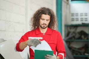 Mechanical man with a checklist inspecting car parts stock in garage warehouse, Young mechanic working in auto repair shop photo