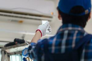 Close up of technician hand turn on air conditioner with remote control, repairman fixing air conditioner unit, Maintenance and repairing concepts photo