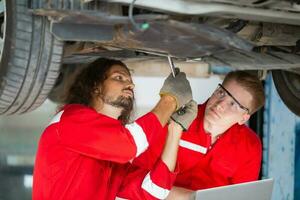 joven mecánica equipo en uniforme son trabajando en auto Servicio con levantado vehículos coche reparar y mantenimiento conceptos foto