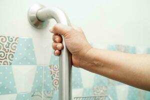 Asian woman patient use toilet support rail in bathroom, handrail safety grab bar, security in nursing hospital. photo