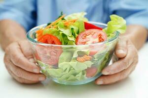 Asian elderly woman patient eating salmon stake and vegetable salad for healthy food in hospital. photo