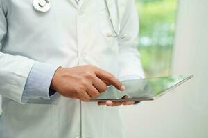 Asian man doctor using tablet computer to reading patient report, check up and search for solve treatment health medical online in hospital. photo