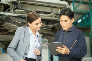 Mechanic and young woman client talking together at the repair garage, Female manager and auto mechanic in auto repair shop, Car repair and maintenance concepts photo