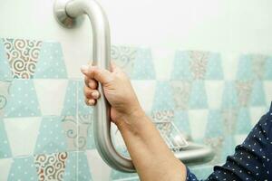 Asian woman patient use toilet support rail in bathroom, handrail safety grab bar, security in nursing hospital. photo