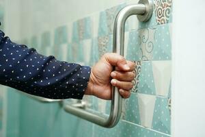 Asian woman patient use toilet support rail in bathroom, handrail safety grab bar, security in nursing hospital. photo